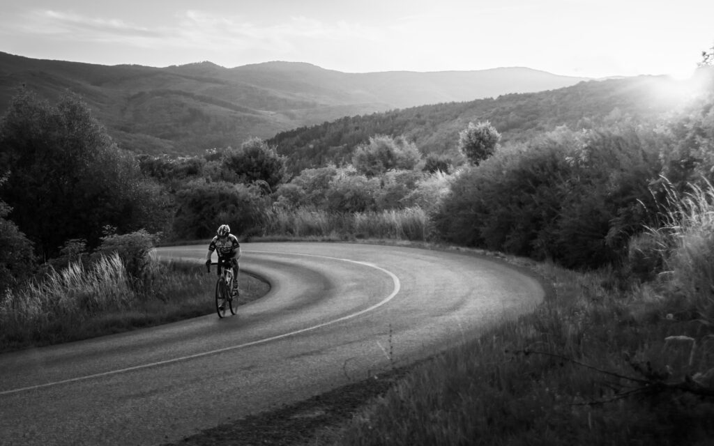a black and white photo of a cyclist riding up a hill
